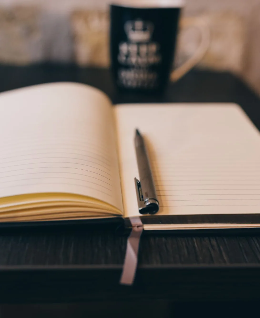 Carnet ouvert avec un stylo posé sur un bureau, à côté d’un ordinateur portable et d’une tasse