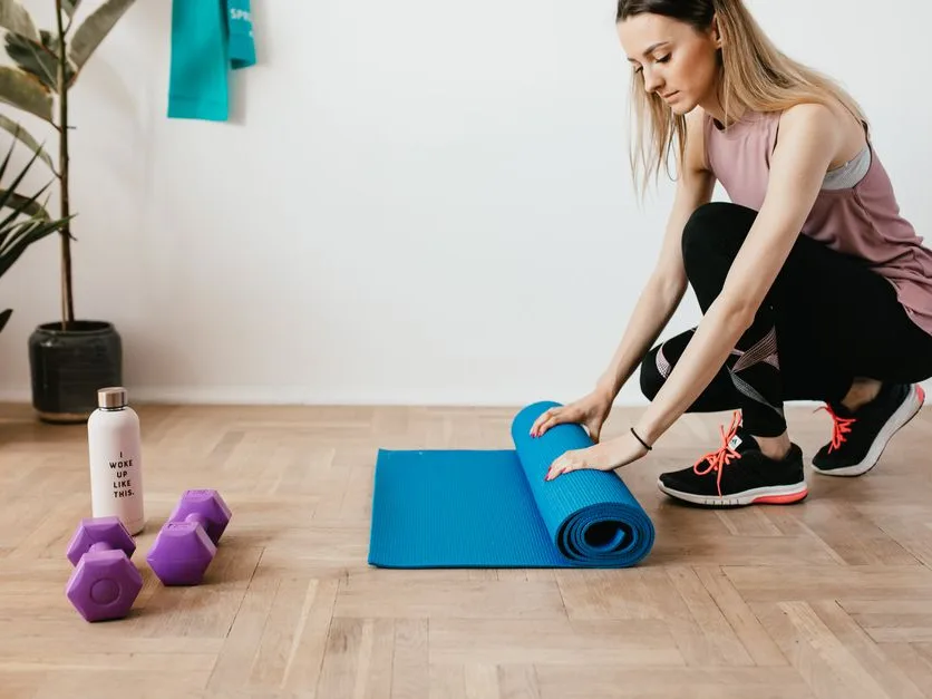 Sportive assise sur son tapis de sol qu’elle déroule dans son salon, haltères et gourde posés à côté