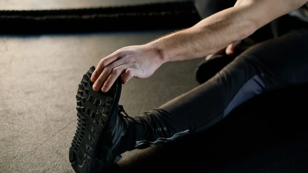 Gros plan d'une main qui attrape le pied d'un sportif assis au sol pour étirer sa jambe