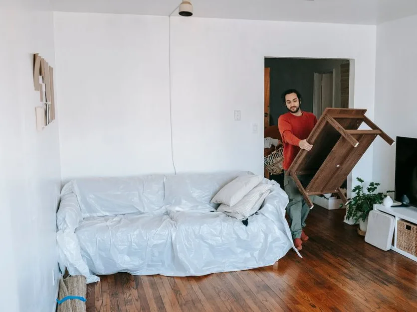 Homme qui soulève une table basse en bois pour libérer de la place dans un salon clair