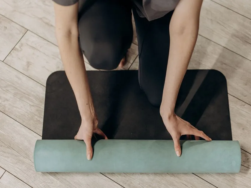 Mains qui déroulent un tapis de sport sur un parquet en bois