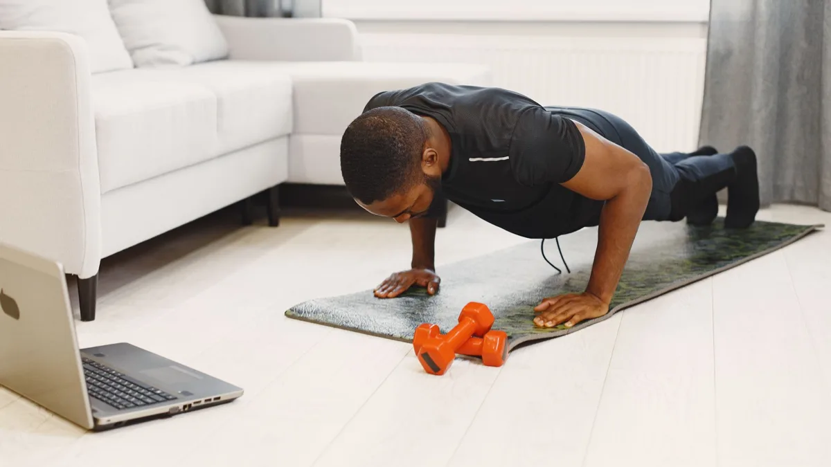 Homme qui fait des pompes sur un tapis dans un salon, avec des haltères orange à côté