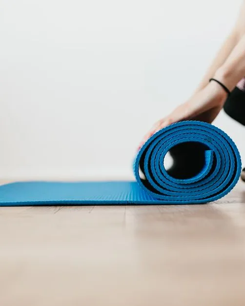 Femme en leggings noirs qui déroule un tapis de sport au sol, dans une pièce dégagée