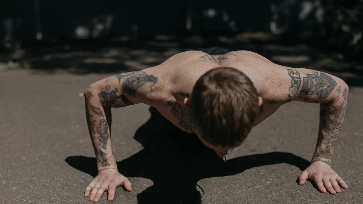 Homme tatoué en position basse de pompe sur le bitume, vu de face, la tête baissée