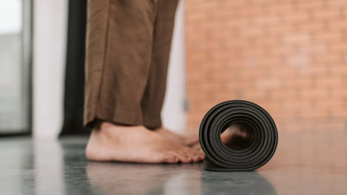Tapis de sol noir roulé devant un mur de briques, à côté des pieds nus d'une personne